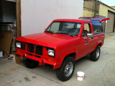 1988 Ford Bronco II - This red 1988 Ford Bronco II is parked in front of a garage with its front grille removed.