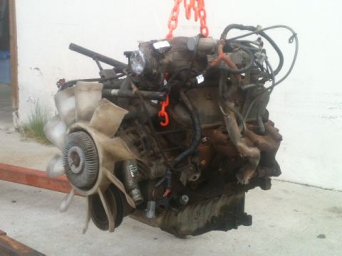 1988 Ford Bronco II - Engine assembly hoisted by chains, showing fan, hoses, and exhaust manifold.