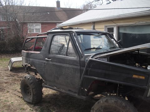 1986 Ford Bronco - Modified black Ford Bronco with a roll cage and off-road tires sits in a yard with the hood open.