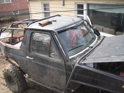 1986 Ford Bronco - This heavily modified SUV features an extensive roll cage and appears to be undergoing some form of customization or repair.