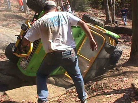 1996 Ford Bronco - An off-road vehicle has become stuck and tipped over on a rocky trail, with a person attempting to help.