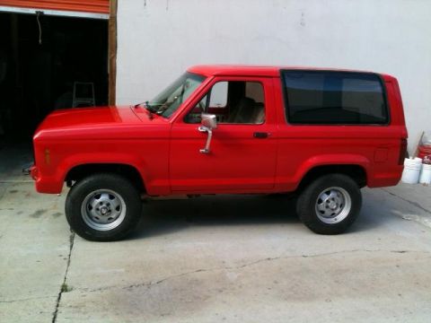 1988 Ford Bronco II - A red 1988 Ford Bronco II is parked outside a garage with its side facing the camera.