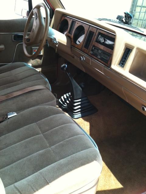 1988 Ford Bronco II - The interior of a vehicle features tan upholstery, a wood-grain dashboard, and a manual transmission shifter.