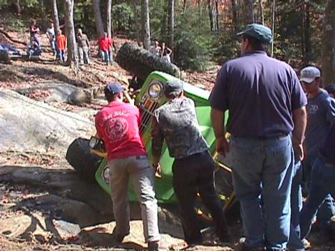 1996 Ford Bronco - People attempt to right an overturned green off-road vehicle in a wooded area.