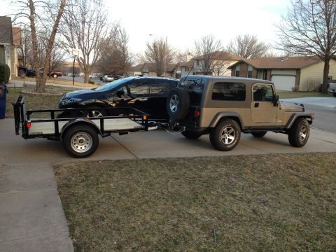 2005 Jeep Wrangler - A tan 2005 Jeep Wrangler is seen towing a trailer that carries a black SUV.