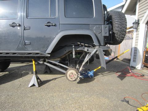 2008 Jeep Wrangler - The rear suspension of a gray Jeep Wrangler is elevated on jack stands, with a blue hydraulic jack positioned beneath the axle for maintena…