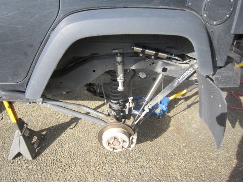 2008 Jeep Wrangler - Jeep Wrangler rear suspension components, including shock mount and sway bar, are visible while the vehicle is supported by jack stands.