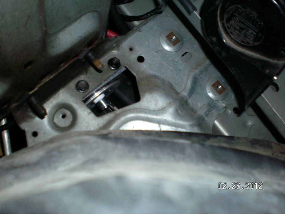 Close-up of a metal bracket with bolts and a small silver cylinder, showing rust and wear