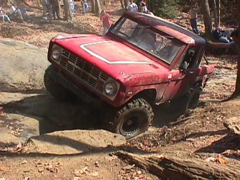 1996 Ford Bronco - This red SUV is navigating a rocky trail with spectators observing the off-road action.