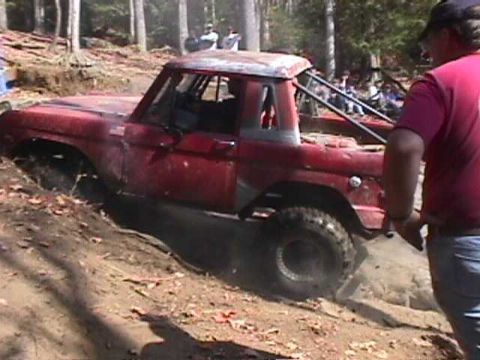 1996 Ford Bronco - A red off-road vehicle navigates a challenging muddy terrain, with a person observing from the side.