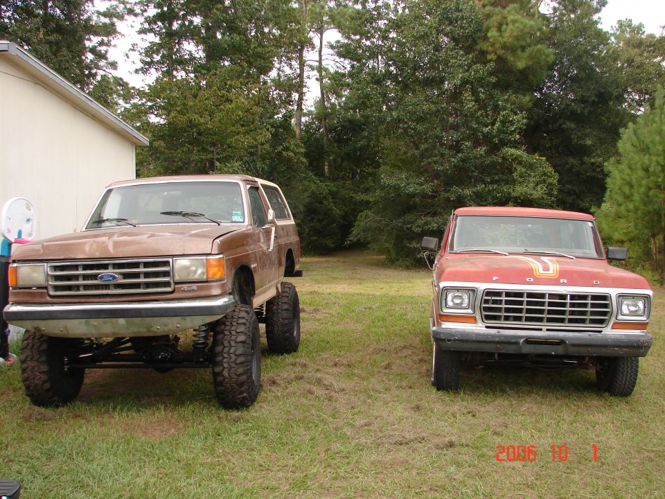 Lifted brown 1978 Ford Bronco and red 1978 Ford pickup truck parked in a grassy yard