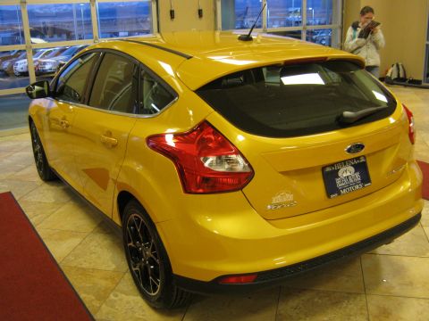 2012 Ford Focus - Rear view of a yellow 2012 Ford Focus hatchback, seen indoors with a dealership license plate frame.