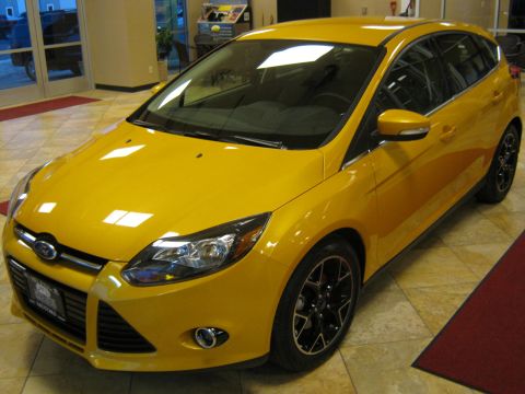 2012 Ford Focus - A yellow 2012 Ford Focus hatchback is shown from a three-quarter front angle inside a showroom.