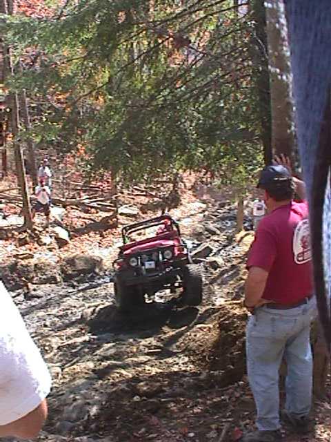 1996 Ford Bronco - A red off-road vehicle tackles a challenging rocky path in a wooded area.