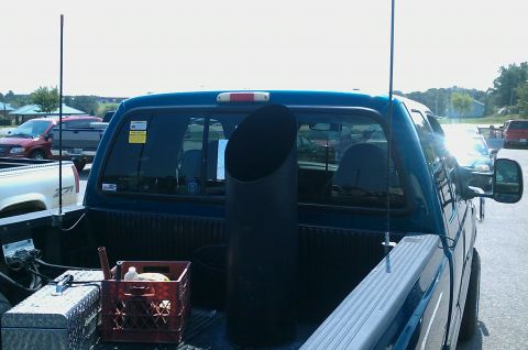 1987 Ford Bronco - A large, black exhaust pipe is visible in the bed of a pickup truck, alongside two antennas and a red crate.