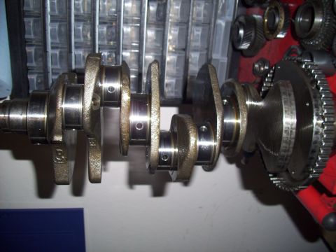 2003 Hyundai Tiburon - A crankshaft with a gear is shown in a workshop setting, with storage bins visible behind it.