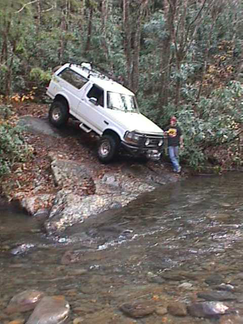 1996 Ford Bronco - 1996 Ford Bronco navigating a rocky stream bed in a wooded area.
