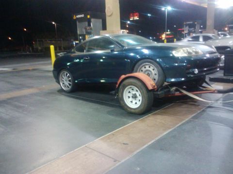 2003 Hyundai Tiburon - 2003 Hyundai Tiburon being towed on a trailer at a gas station.