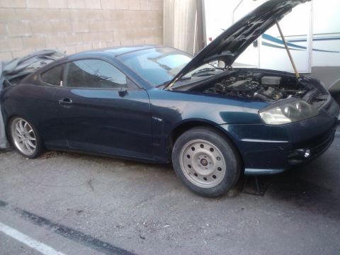 2003 Hyundai Tiburon - A dark blue 2003 Hyundai Tiburon is parked with its hood open, revealing the engine bay.