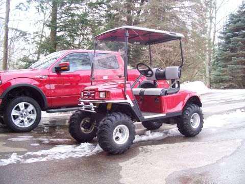 1978 Ford F-150 - A red golf cart equipped with off-road tires is positioned beside a red pickup truck on a wet, snowy surface.