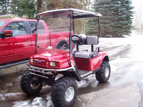 1978 Ford F-150 - Golf cart with large tires sits beside a red pickup truck in a snowy outdoor setting.