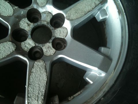 2000 Jeep TJ - Close-up of a silver Jeep wheel, showing lug nut holes and tire sidewall with debris.