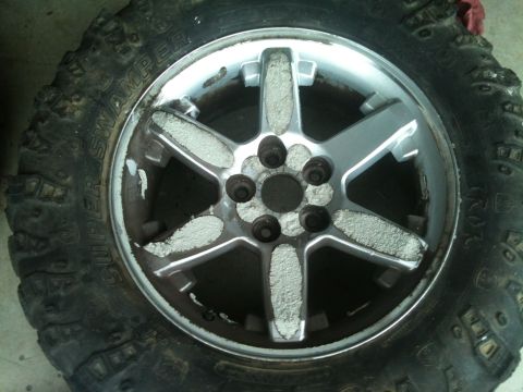 2000 Jeep TJ - A close-up view of a wheel and tire assembly, showing a silver 5-spoke rim with white residue and a Super Swamper tire.