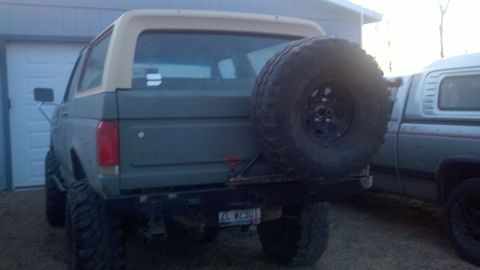 1989 Ford Bronco - A lifted Ford Bronco with a spare tire on the back is parked next to a pickup truck.