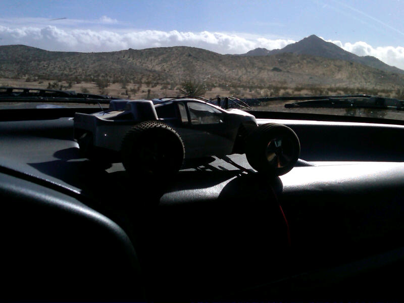 toy monster truck on dashboard with desert mountains outside