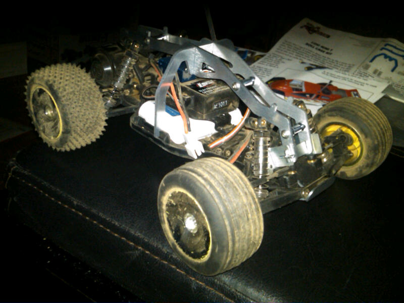 RC car chassis with exposed electronics and suspension parts. Instructions are visible in the background