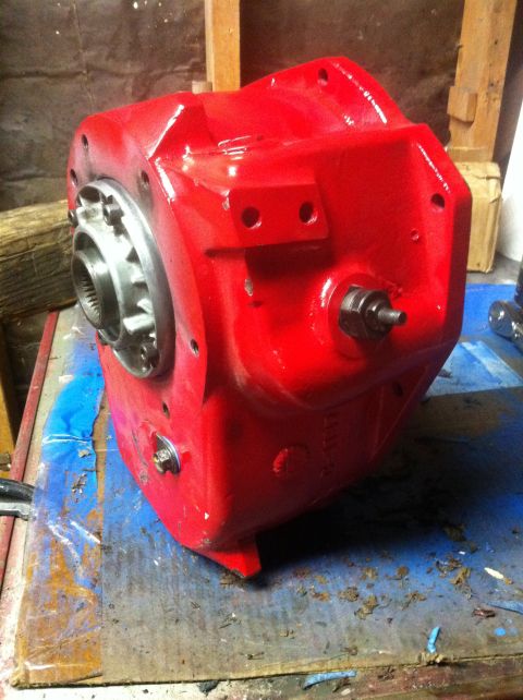 1989 Ford Bronco - A red painted transfer case sits on a workbench, showing its splined input shaft and various bolt holes.