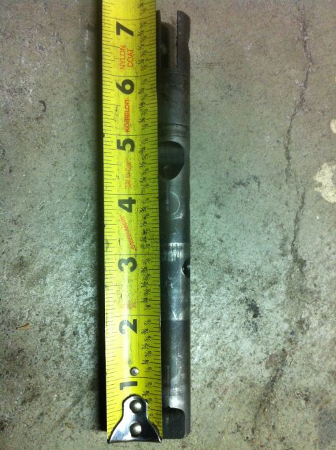 1989 Ford Bronco - A metal shaft is measured against a tape measure, indicating its length.
