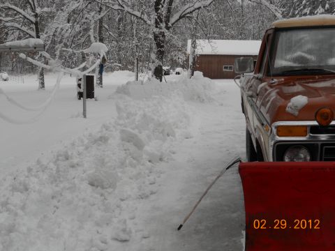1978 Ford Bronco - A snow-covered orange pickup truck is equipped with a red snow plow, ready for winter conditions.