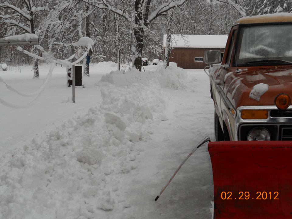 orange pickup truck with snow plow in front, parked in snow
