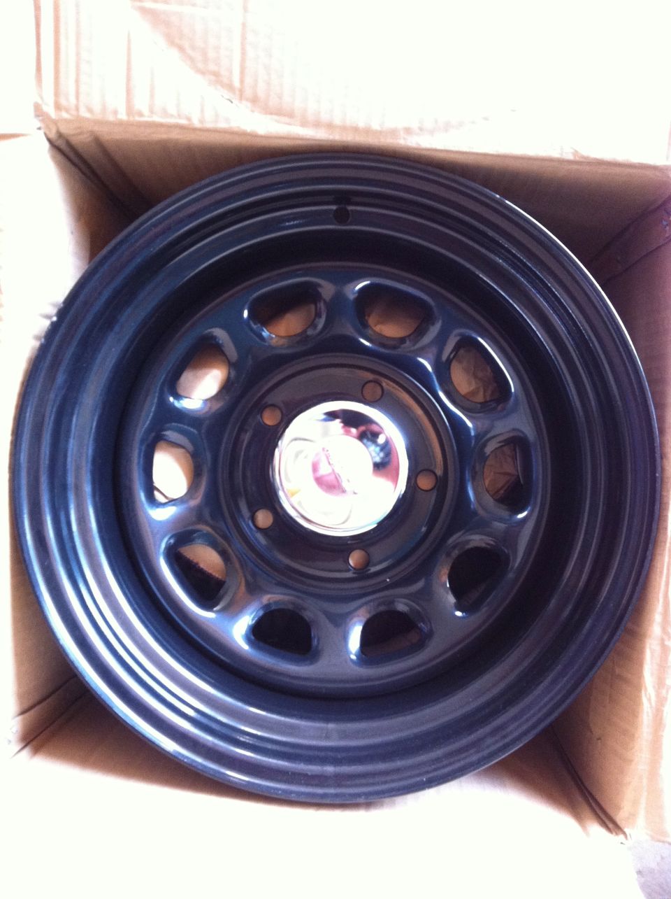 Dark gray steel wheel with chrome center cap in a cardboard box.