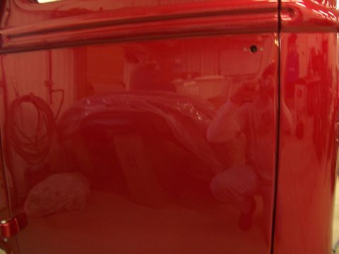 1978 Ford F-150 - A reflection of a person is visible on the glossy red paint of a vehicle door.