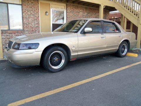 2000 Mercury Grand Marquis - Side view of a tan sedan with aftermarket wheels parked in a lot.