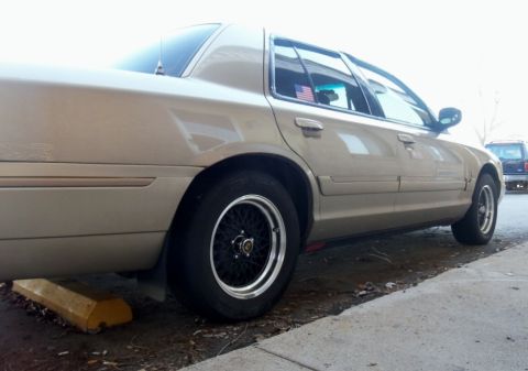2000 Mercury Grand Marquis - Side view of a tan sedan with custom wheels parked next to a curb.