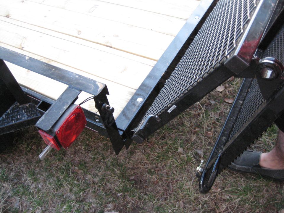 Close-up of a trailer ramp hinge with wooden deck visible