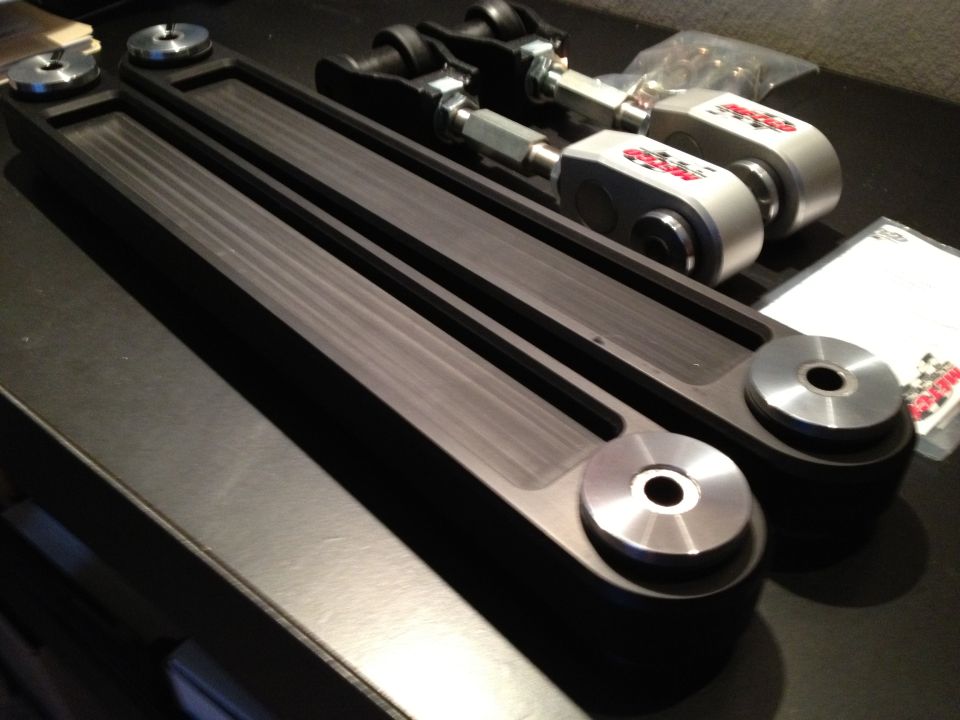 Pair of black aftermarket control arms with silver end links and red logos