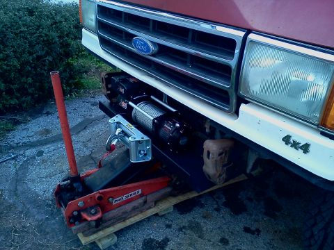 1989 Ford Bronco - A Ford truck's front end is shown with a winch installed, and a floor jack is nearby.