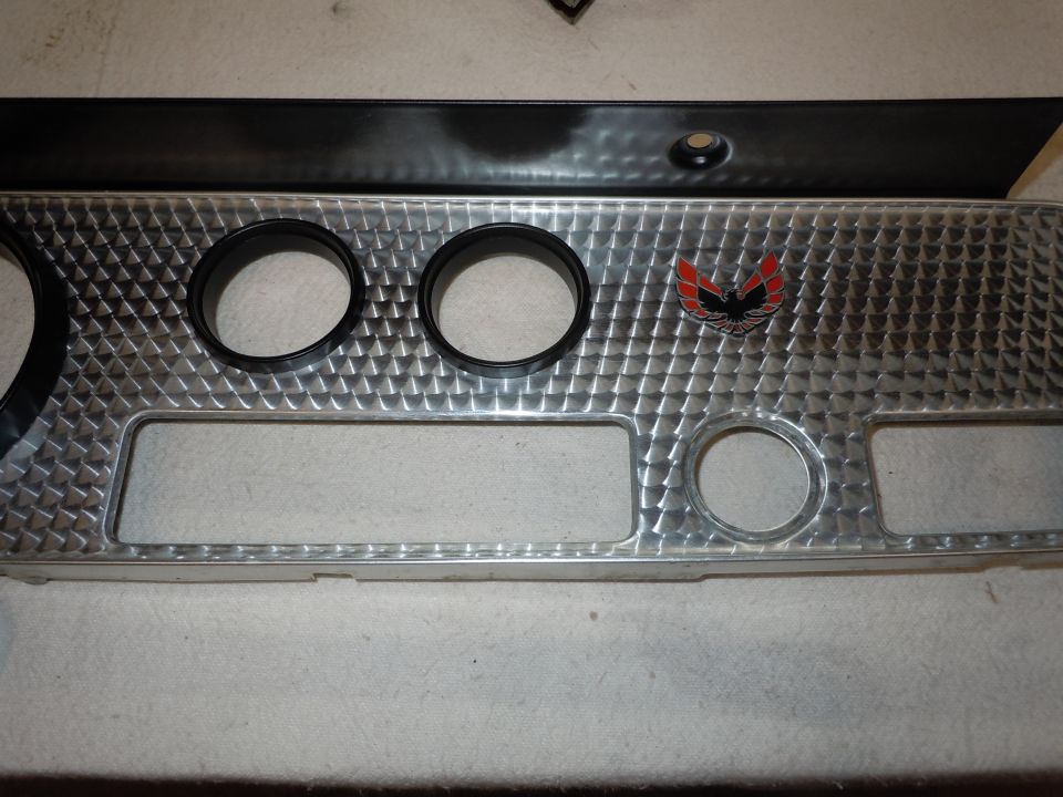 Dashboard trim with two gauge holes, a rectangular cutout, a circular cutout, and a red and black bird emblem. This is from a 1973 Pontiac Trans Am