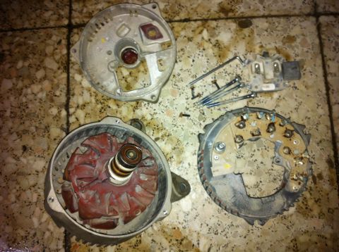 1998 Ford Crown Victoria - Disassembled alternator parts laid out on a tiled surface, with screws nearby.