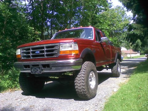 1996 Ford F-250 - This red Ford pickup truck, likely from the early to mid-1990s, is modified with oversized tires and a lifted suspension.