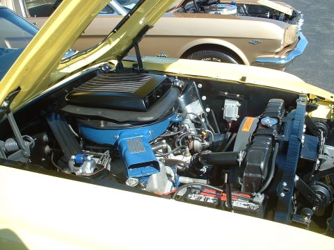 1995 Ford Crown Victoria - The engine compartment of a vintage yellow car is shown, with another classic vehicle in the background.