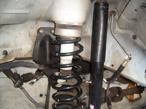 1994 Jeep Cherokee - Close-up view of the front suspension system, revealing the coil spring and shock absorber with visible signs of age and corrosion.