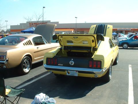1995 Ford Crown Victoria - A yellow 1970 Ford Mustang Mach 1 is parked next to a gold classic car, both with hoods or trunks open.
