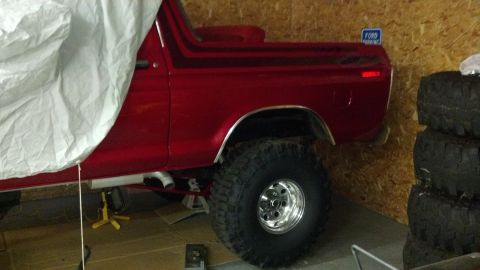 1978 Ford Bronco - A red 1978 Ford Bronco is partially covered, showing its side profile and large off-road tires.