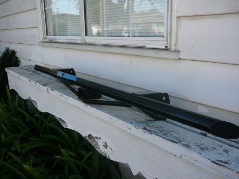 1988 Ford Bronco - A black metal bar with mounting brackets is placed on a weathered white ledge next to a window.