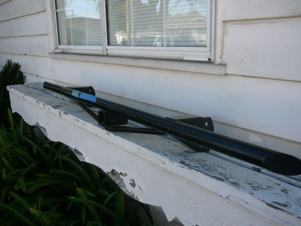 Black metal bar with blue tape and mounting brackets on a weathered white ledge